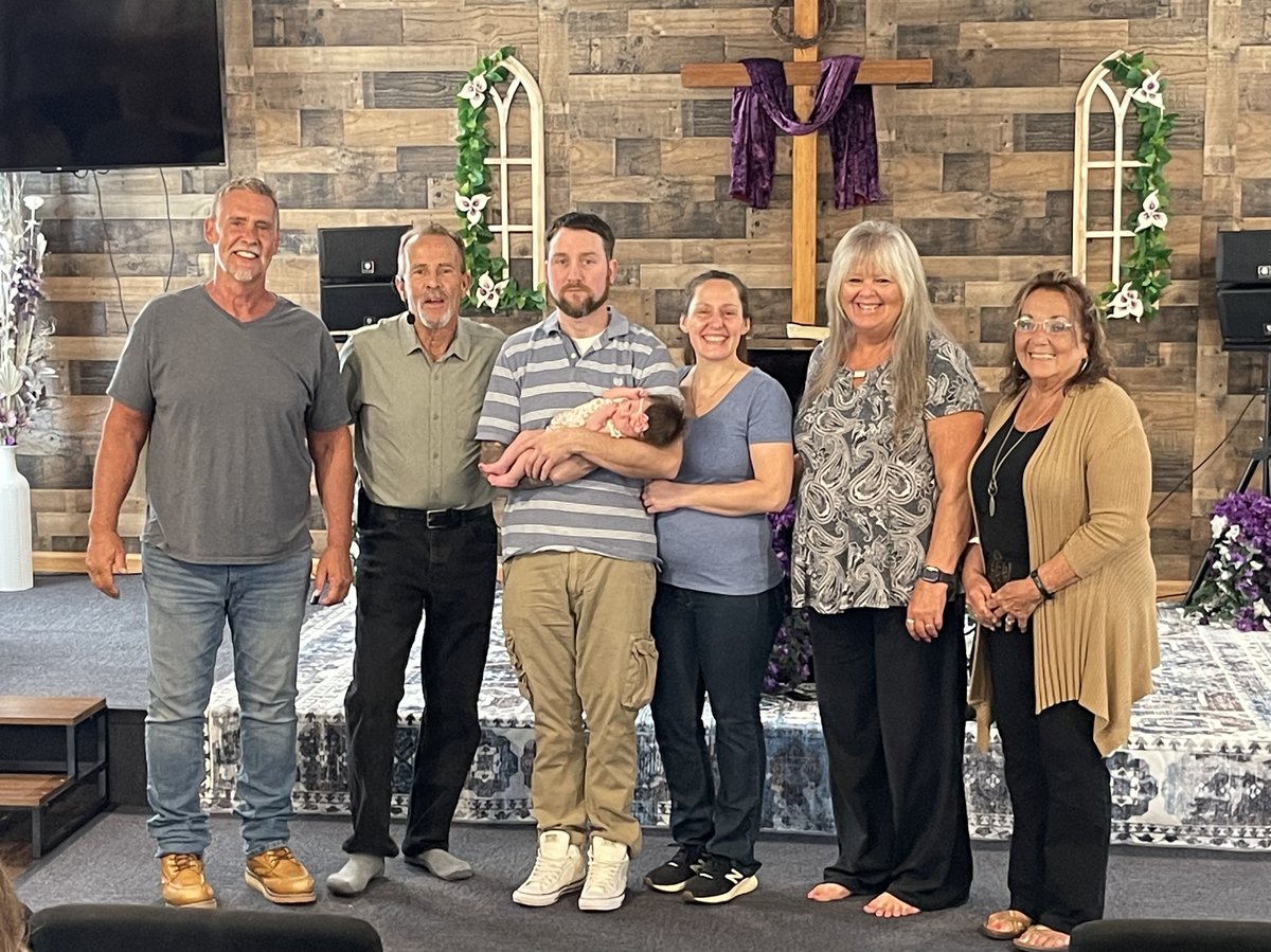 Family gathered on stage around a wooden cross for a baby dedication